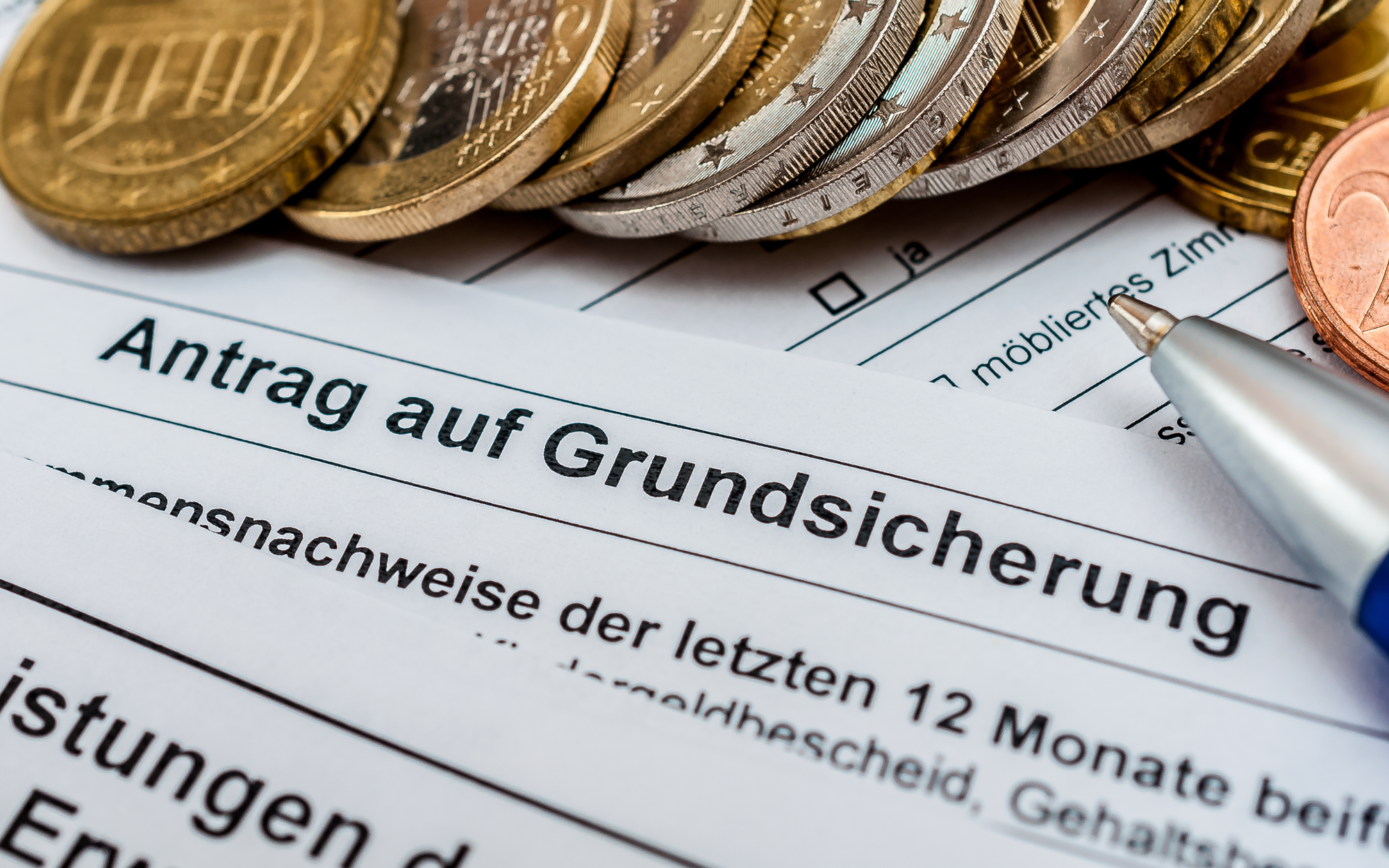 Antrag auf Grundsicherung im Alter mit Geldmünzen und Kugelschreiber als Symbol für finanzielle Unterstützung.