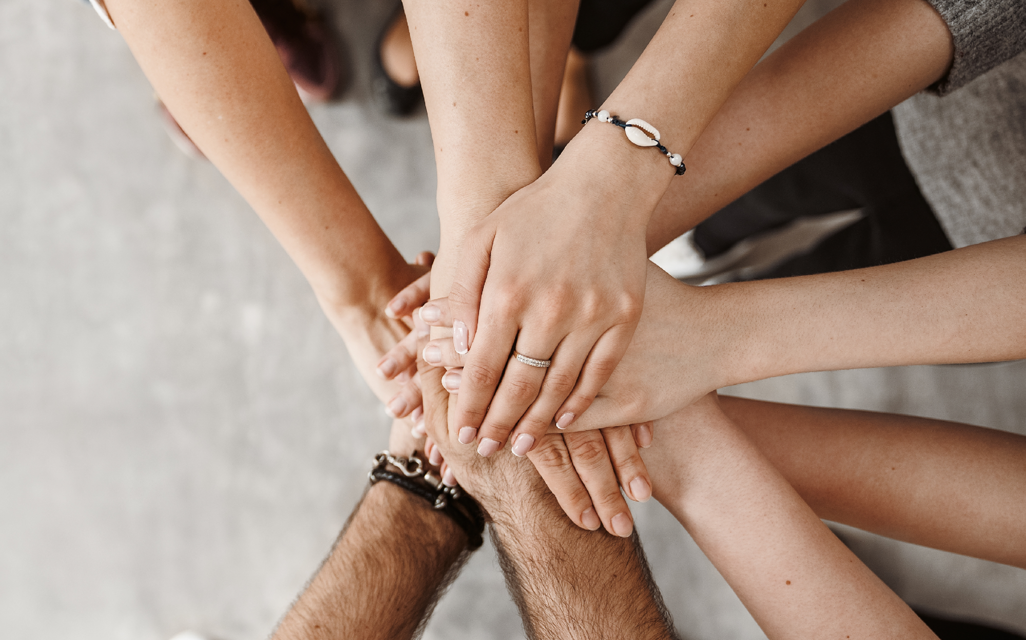 Mehrere Hände unterschiedlicher Personen liegen übereinander, symbolisieren Teamarbeit und Zusammenhalt. Daneben der Text „NIMM DEINE KARRIERE IN DIE HAND!“ als motivierender Aufruf zur aktiven Gestaltung des eigenen Berufsweges.