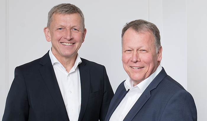 Geschäftsführung Stadtwerke Winterberg Energie, beginnend von links: Norbert Menke und Henrik Weiß. Beide stehen vor einem neutralen Hintergrund und lächeln in die Kamera.