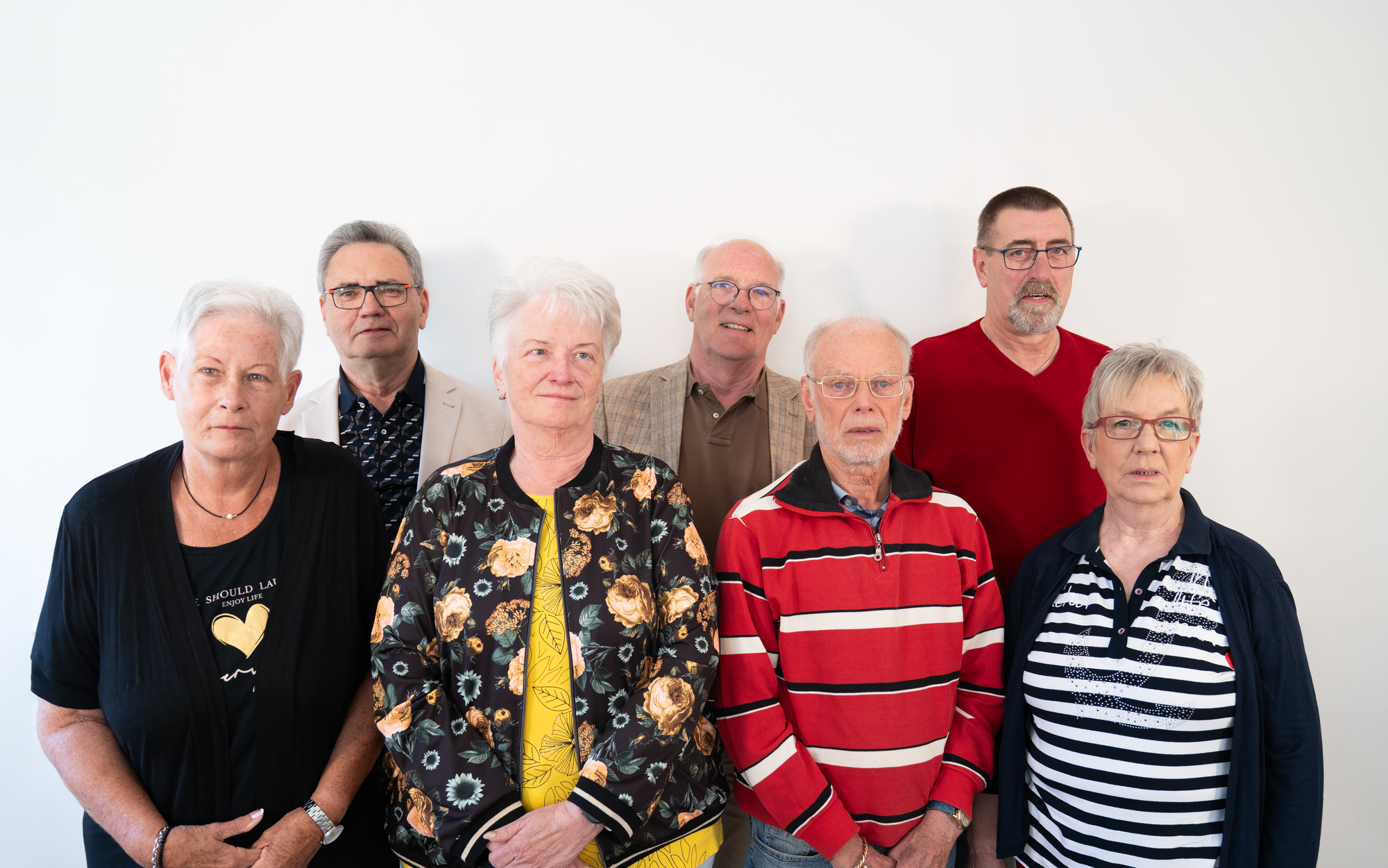 Gruppenportrait des Seniorenbeirats vor weißem Hintergrund. Die Mitgliederinnen und Mietglieder stehen in einer Reihe und blicken freundlich in die Kamera. Alle Personen sind gut sichtbar und einheitlich ausgeleuchtet.